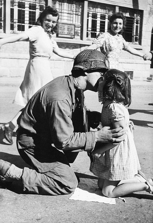 Kiss of Liberation: Sergeant Gene Costanzo kneels to kiss a little girl during spontaneous celebrations in the main square of the town of St. Briac, France, August 14, 1944