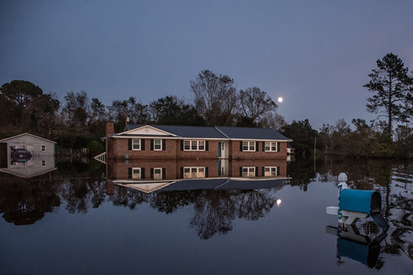 A home illuminated by moonlight sits still in the water of a flooded community at Rocky Point, 2018