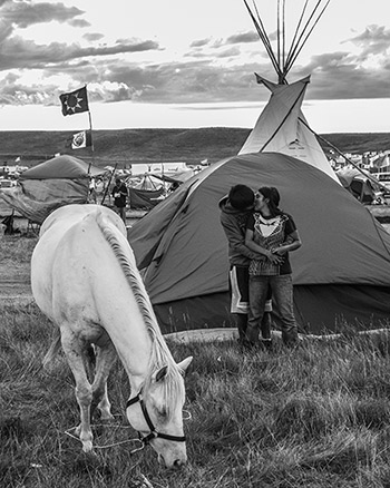 Hiding from view of nearby families, a young couple sneaks in a quick kiss while allowing a horse to graze on Oceti Sakowin grass, September 8, 2016