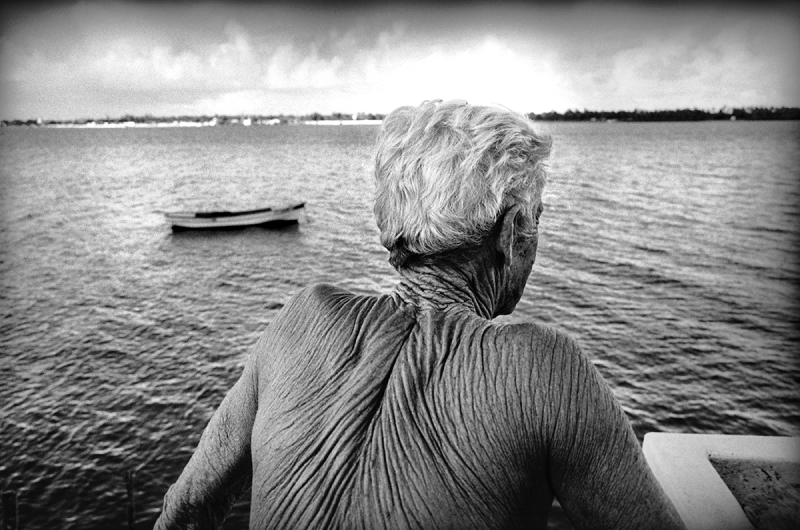Ze Peixe or “the fish,” looks out at the Sergipe River in Aracaju, Brazil, 2002. He is Brazil’s most famous boat pilot, Guiding ships into and out of the harbor, he returns to shore by swimming, and has never worn shoes. Archival Pigment Print