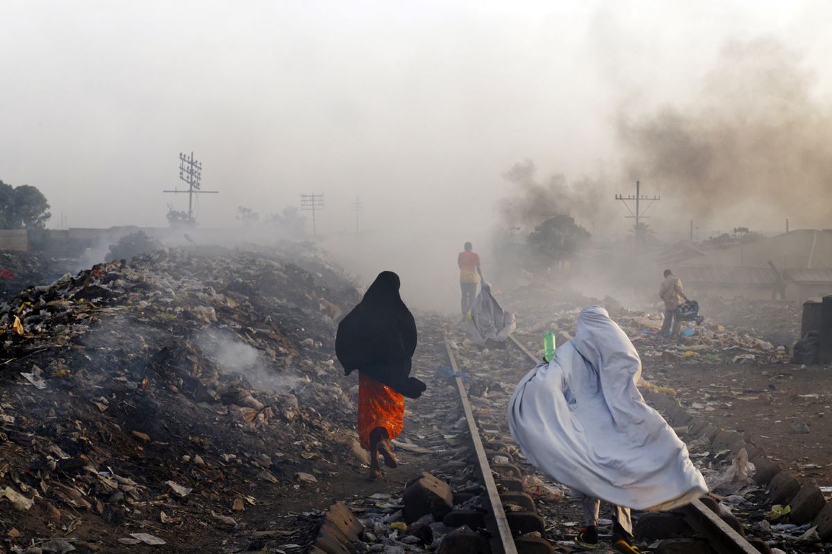 Locals go about their routis, stepping over garbage heaps that burn along the railroad tracks, Kaduna, Nigeria, 2013