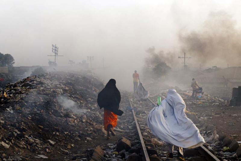 Locals go about their routis, stepping over garbage heaps that burn along the railroad tracks, Kaduna, Nigeria, 2013<br/>Please contact Gallery for price