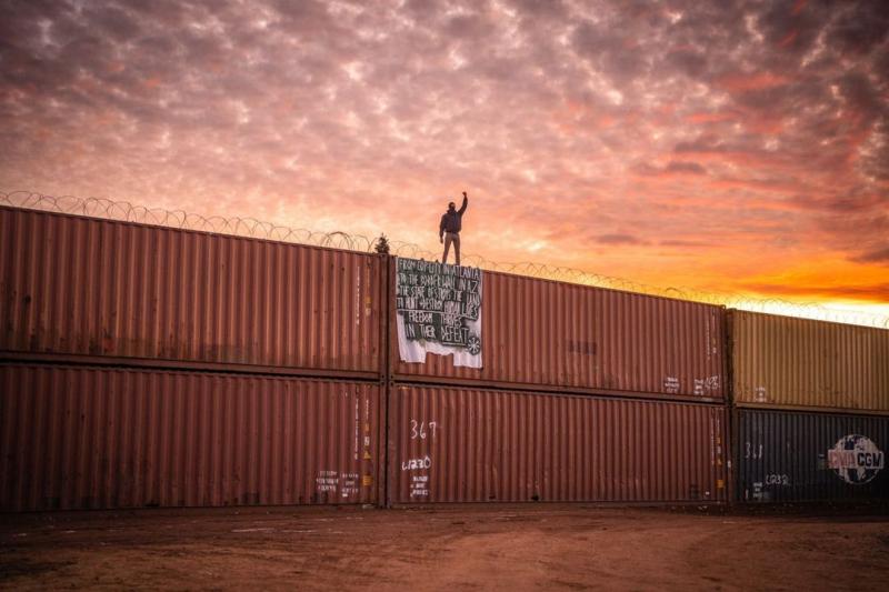Protestor on illegal wall of shipping containers straddling the AZ / Mexico border , December, 2022<br/>Please contact Gallery for price