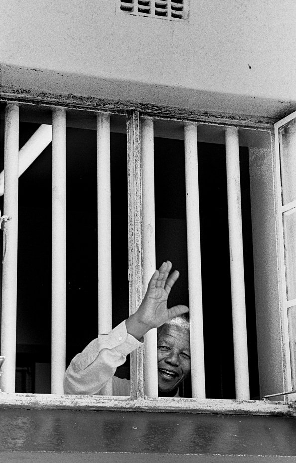 Nelson Mandela waving through prison bars of his former cell during revisit to Robbn Island, 1994