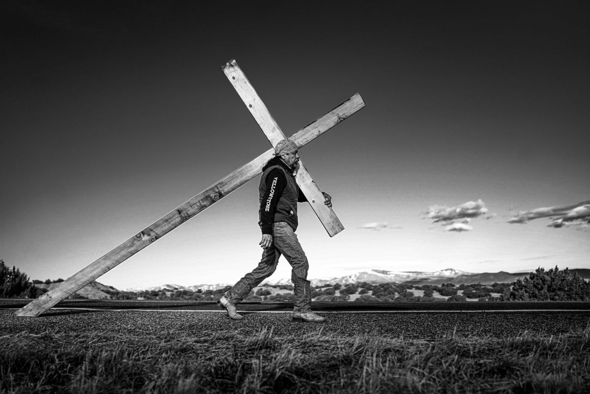 A man  carries a large wooden cross down N.M. 503 for the annual Good Friday pilgrimage to the Santuario de Chimayo, 2024