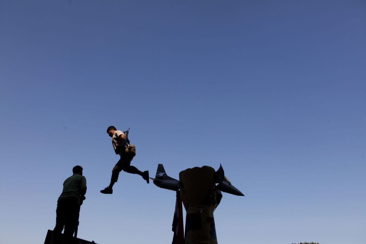 A rebel soldier jumps off a statue of a fist crushing an American plane at Bab al-Aziziya, the  compound of Col. Muammar el-Qaddafi. Tripoli, Libya, 2011