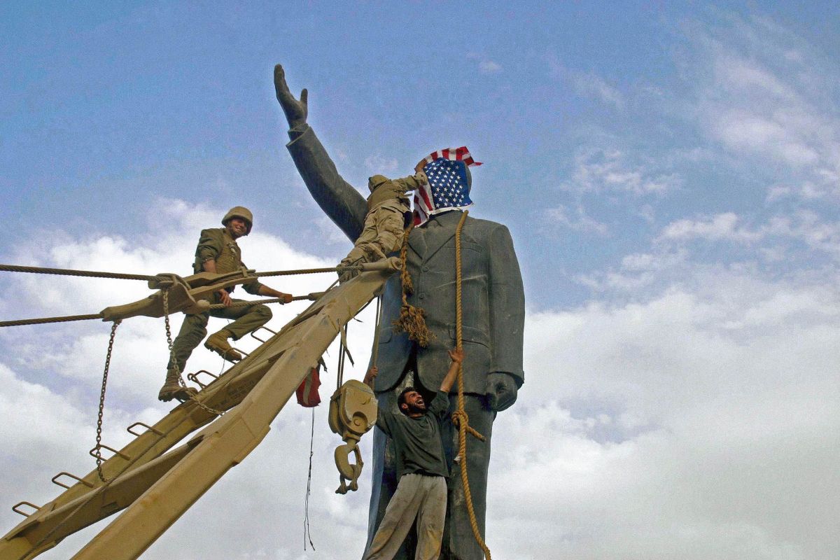 A U.S. Marine covers the face of a statue of Saddam Hussein with a U.S. flag before the statue  was toppled. Baghdad, Iraq 2003