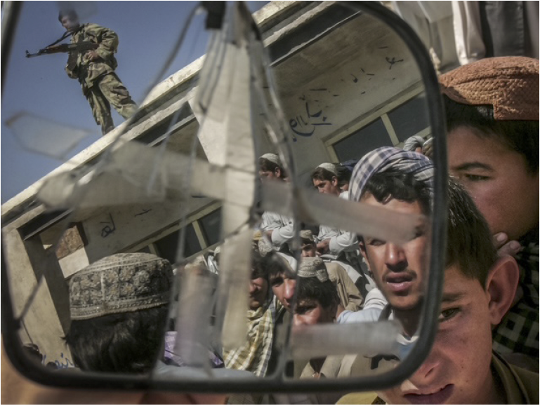 Photo: An armed guard is seen reflected in a broken car mirror as he stands watch at a polling station in Afghanistan during the U.S. post-9/11 occupation. Archival Pigment Print #3077