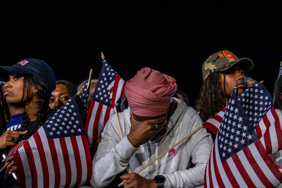 olor photograph of African-American woman with her head in her hands surrounded by American flags as supporters of Vice President Kamala Harris react to results on election night. Washington D.C
