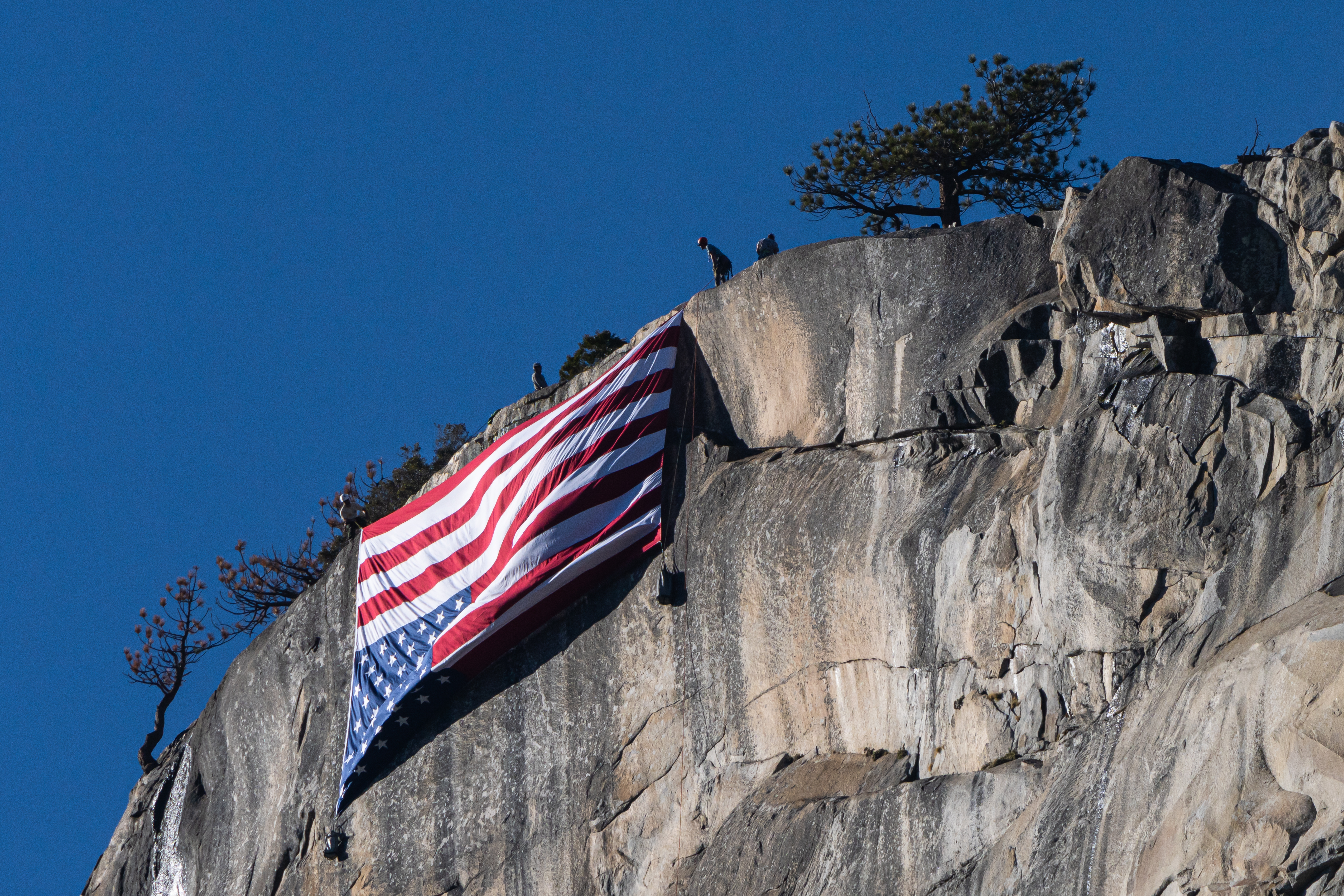 color photograph of an inverted American flag — historically used as a sign of distress — off the side of El Capitan, a towering rock formation in Yosemite National Park, hung to protest the Trump administration’s cuts to the National Park Service in 2025