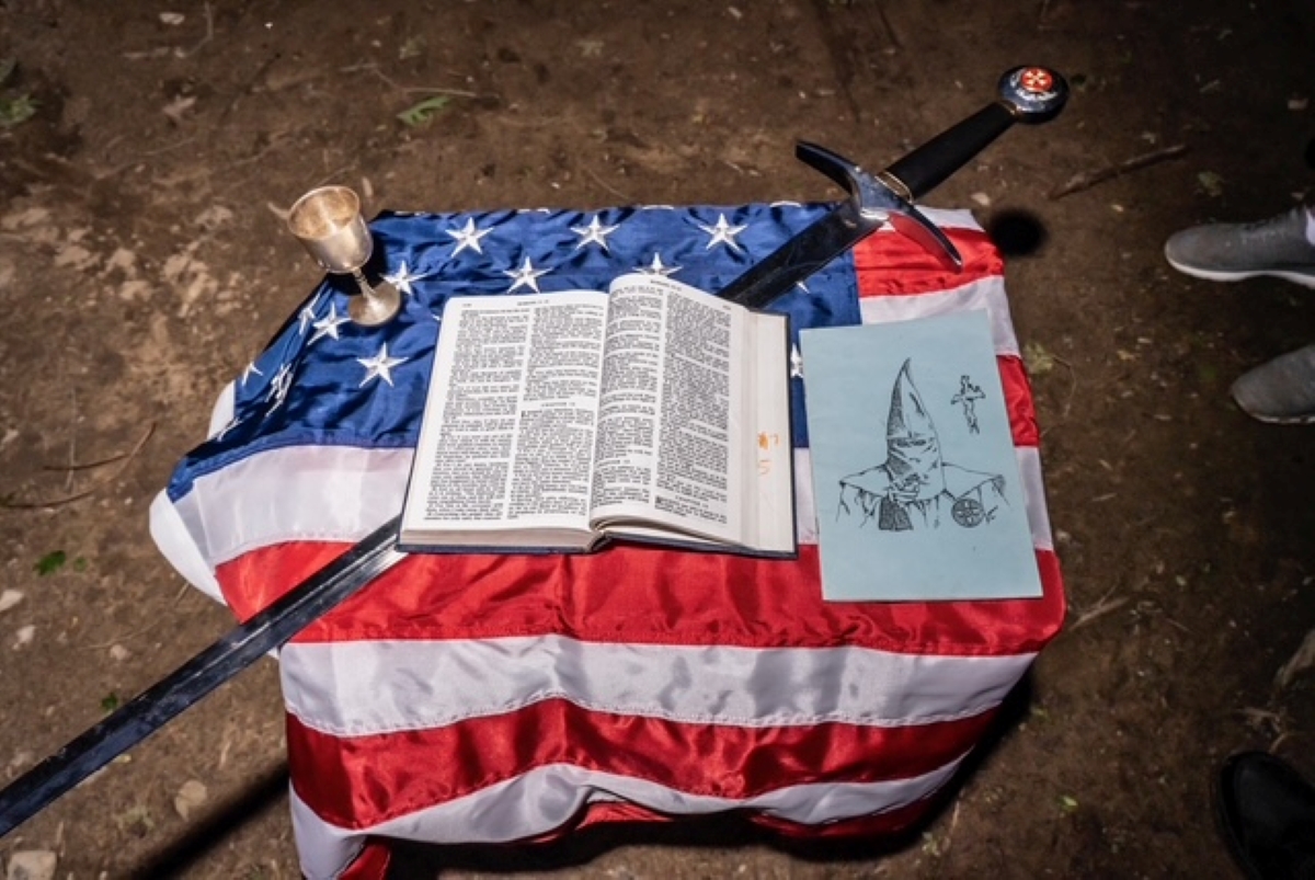 color photograph of an American Flag covered table with a bible, sword, chalice, and KKK material during a Klan New Member Meeting, Kentucky, May, 2025
